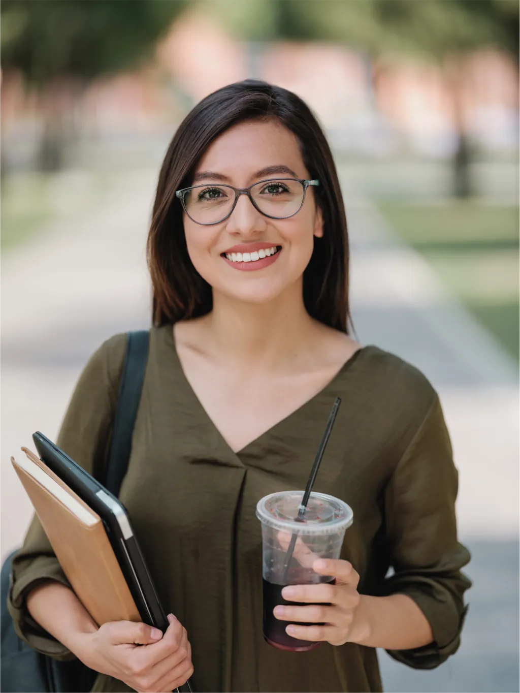 Young woman holding books and a drink, smiling